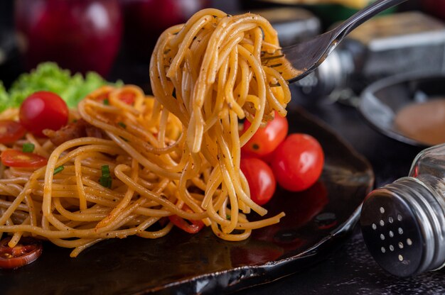 Spaghetti in una tazza nera con pomodori e lattuga.