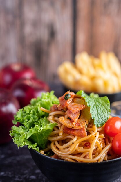 Spaghetti in una tazza nera con pomodori e lattuga.