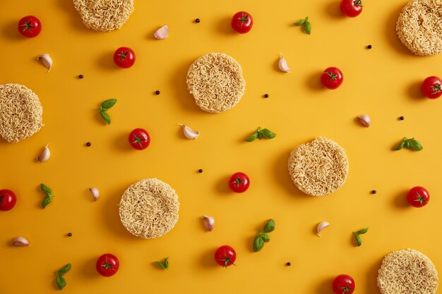 Spaghetti istantanei secchi con pomodori, aglio, basilico e pepe per preparare zuppa fresca, sfondo giallo. Preparare il pranzo veloce. Mangiare malsano e concetto di fast food. Ingredienti per preparare il piatto