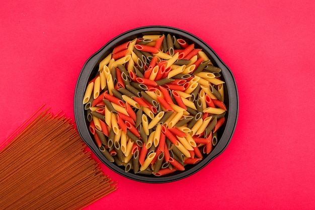 spaghetti marroni e pasta di colore diverso in ciotola nera sulla superficie rosa