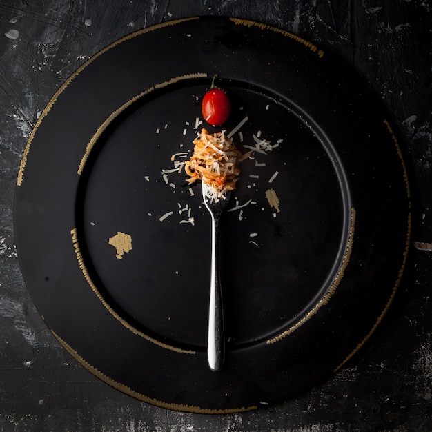 Spaghetti vista dall'alto con forchetta e pomodoro e ricotta in banda nera rotonda