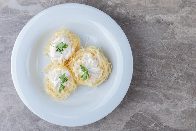 Spaghetti, yogurt e verdura verde nel piatto, sul marmo.