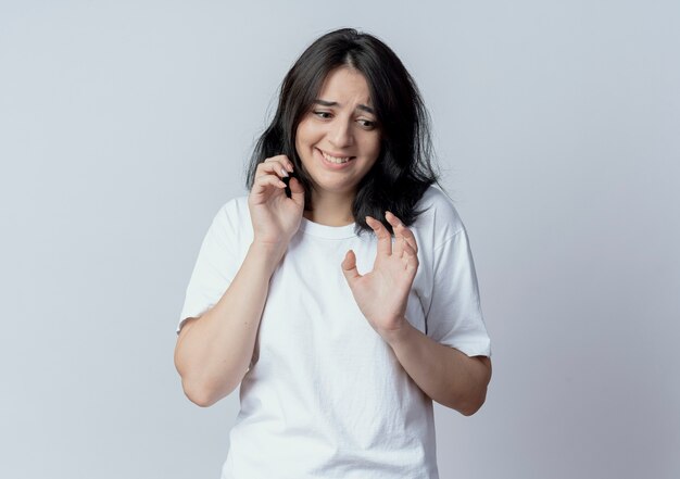 Spaventata giovane ragazza abbastanza caucasica guardando verso il basso e tenendo le mani in aria non gesticolando isolato su sfondo bianco con spazio di copia