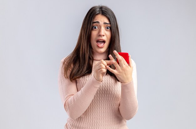 Spaventata guardando la telecamera giovane ragazza il giorno di san valentino tenendo l'anello nuziale isolato su sfondo bianco