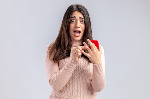 Spaventata guardando la telecamera giovane ragazza il giorno di san valentino tenendo l'anello nuziale isolato su sfondo bianco