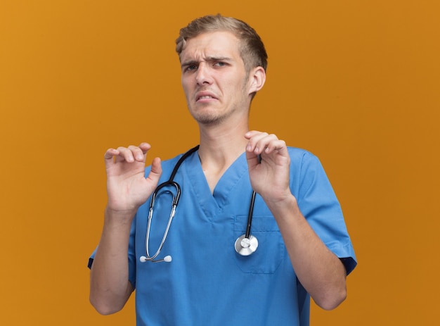Spaventato il giovane medico maschio che indossa l'uniforme del medico con lo stetoscopio isolato sulla parete arancione