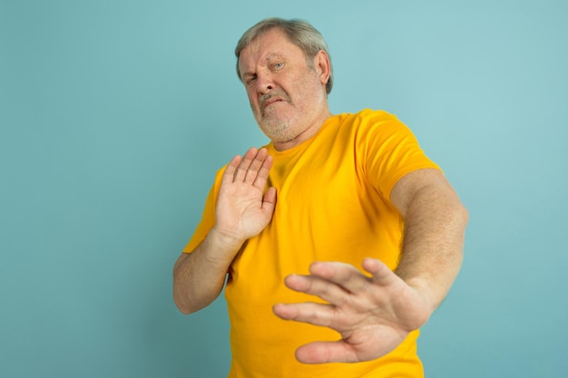 Spaventato, rifiutando. Ritratto di uomo caucasico isolato su sfondo blu studio. Bello modello maschio in posa gialla della camicia.