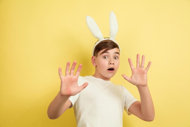 Spaventato, scioccato. Ragazzo caucasico come un coniglietto di Pasqua su sfondo giallo studio. Auguri di buona Pasqua.