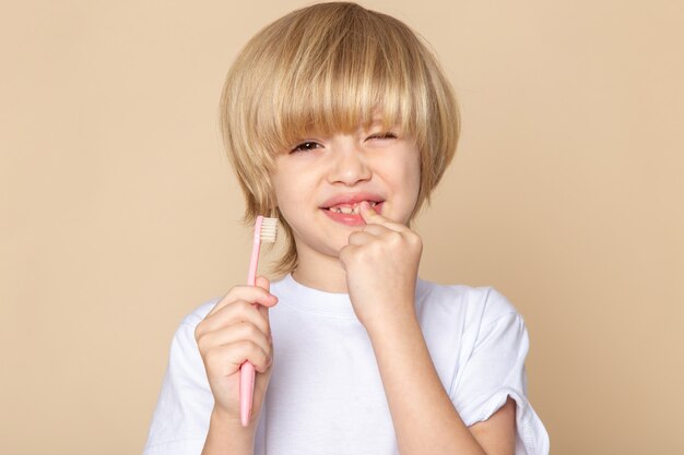 spazzolino da denti dolce della tenuta del ragazzo sveglio biondo sullo scrittorio rosa