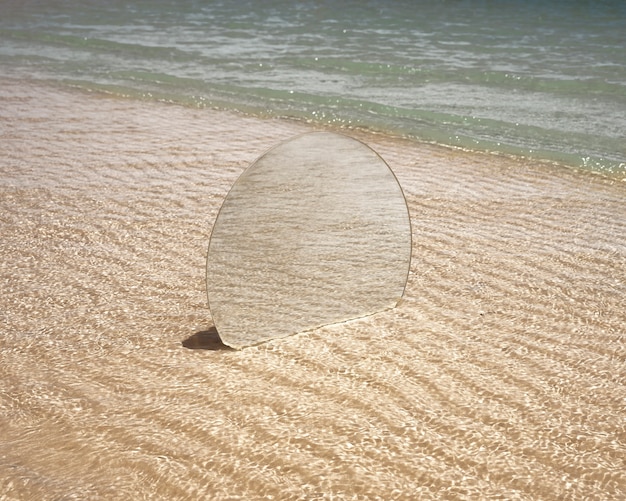 Specchio rotondo in vetro sulla spiaggia che riflette il paesaggio