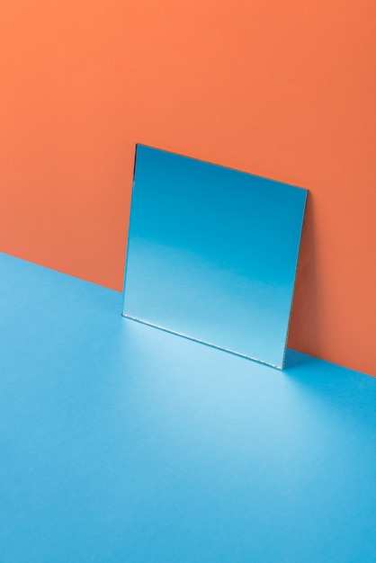 Specchio sulla tavola blu isolata sull'arancia
