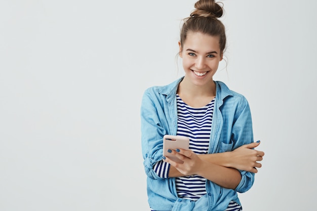 spensierato tenero attraente giovane donna fiduciosa capelli pettinati hairbun sorridente, ridendo divertendosi tenendo smartphone cercando felice ghignando scherzando intorno