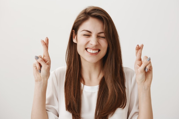 Speranza ragazza positiva incrocia le dita mentre esprime il desiderio, sorridendo ottimista