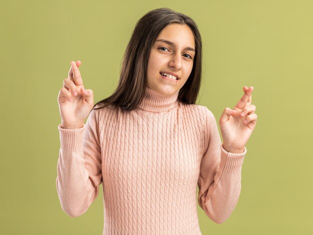 Speranzosa bella ragazza adolescente che guarda la telecamera facendo un gesto di fortuna con entrambe le mani che mordono il labbro isolato sul muro verde oliva