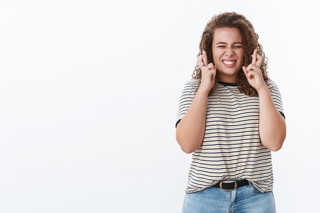 Speranzoso fedele eccitato carino ragazza grassoccia dai capelli ricci stringere i denti entusiasta incrociare le dita buona fortuna in attesa buoni risultati positivi fedelmente desidero che il desiderio si avveri