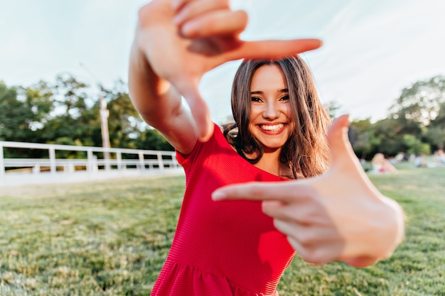 Spettacolare ragazza bruna che gode del servizio fotografico estivo. Magnifica signora con l'espressione del viso felice scherzare nel parco nel fine settimana.