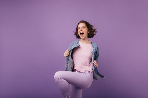 Spettacolare ragazza magra in pantaloni viola che salta con il sorriso. Modello femminile accattivante che esprime felicità.