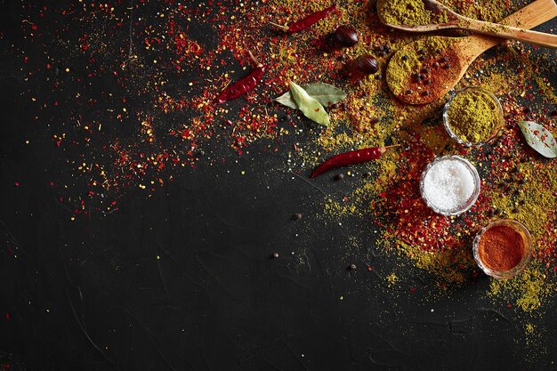 Spezie assortite su sfondo nero scuro. Condimenti per alimenti. Curry, paprika, pepe, cardamomo, curcuma. Vista dall'alto. Avvicinamento. Concetto di spezie. Spezie ingredienti per cucinare