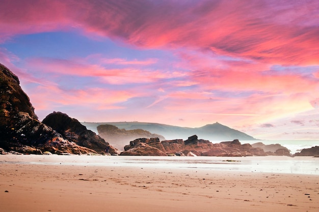 Spiaggia circondata da rocce e mare sotto un cielo nuvoloso durante un bel tramonto rosa