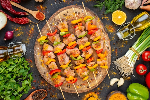 Spiedini di pollo crudo vista dall'alto su tavola di legno naturale e altri oggetti sul tavolo scuro