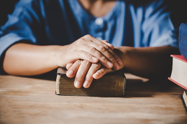 Spiritualità e religione, mani giunte in preghiera su una Sacra Bibbia nel concetto di chiesa per la fede.