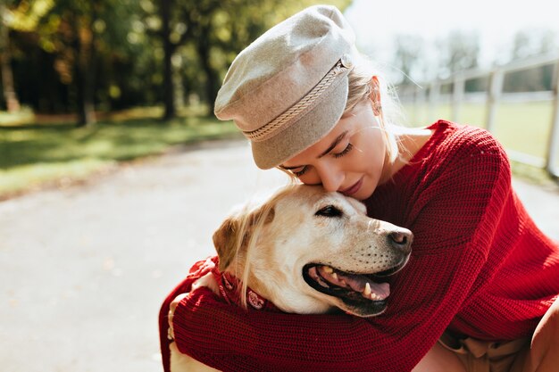 Splendida bionda con il suo amato cane che trascorrono del tempo insieme all'aperto in autunno. Bellissimo ritratto di una giovane donna e il suo animale domestico nel parco.