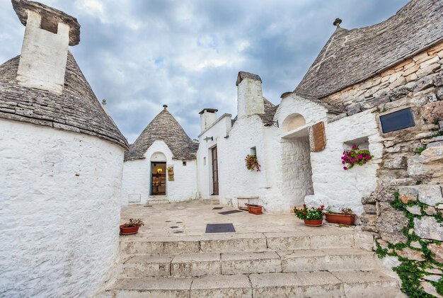 Splendida cittadina di Alberobello con trulli tra piante verdi e fiori, principale distretto turistico, Puglia, Italia meridionale. Tipici edifici imbiancati a calce costruiti con muri a secco e