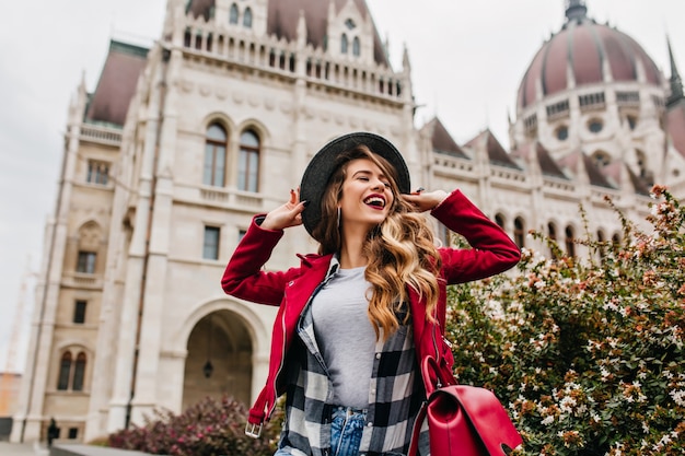 Splendida donna bianca che tocca il suo cappello mentre posa vicino al vecchio luogo storico