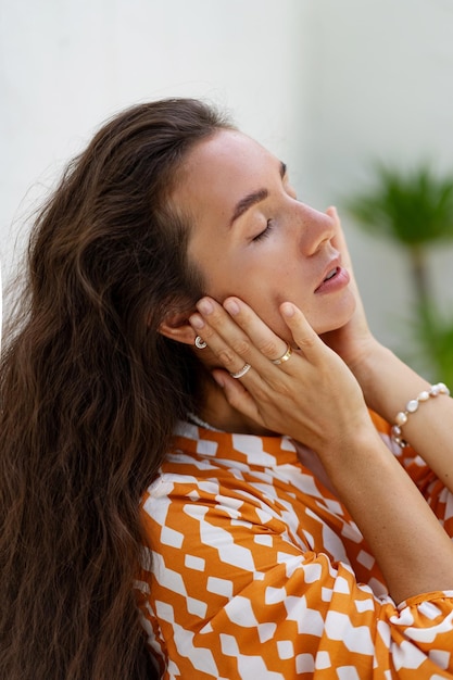 Splendida donna con capelli ondulati perfetti in abito estivo alla moda in posa su sfondo bianco