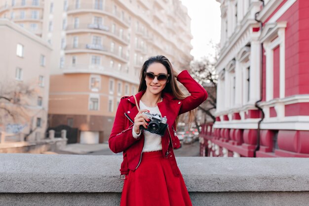 Splendida fotografa femminile in occhiali da sole scuri che giocano con i suoi capelli sullo spazio della città