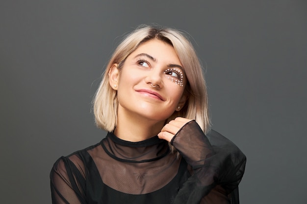 Splendida incredibile giovane donna bionda in abito trasparente, alzando lo sguardo con espressione facciale sognante, sorridendo misteriosamente, esprimendo un desiderio.