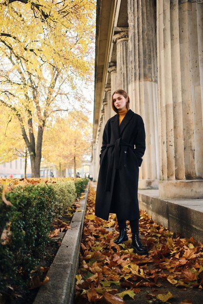 Splendida ragazza alla moda in cappotto nero che riposa nel bellissimo parco cittadino autunnale