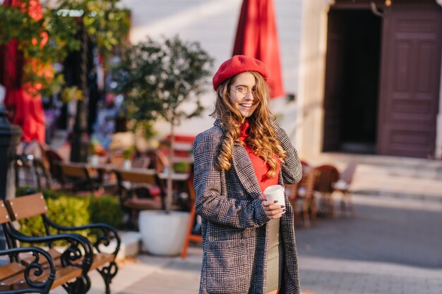 Splendida ragazza bianca in cappotto lungo che beve caffè mentre si cammina nel parco