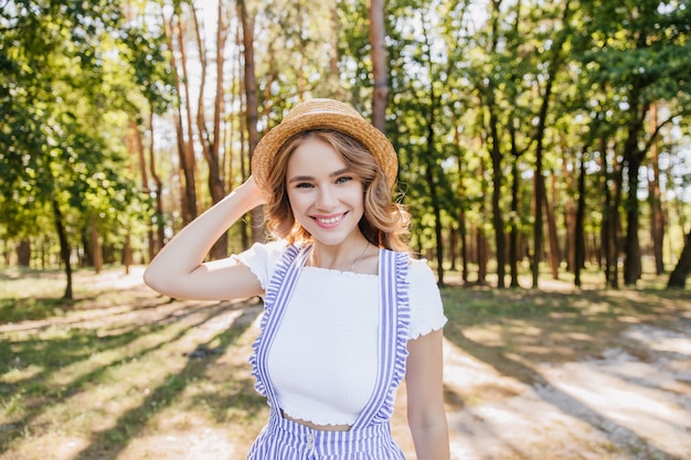 Splendida ragazza riccia in posa nella foresta con un bel sorriso. Colpo all'aperto di giovane signora accattivante che si diverte nel parco nella mattina di sole.