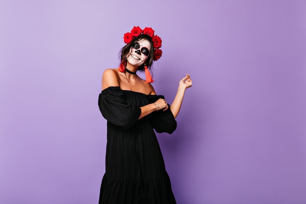 Splendida signora adulta in prendisole neri ballando sulla parete isolata. La ragazza con le rose nei capelli neri ride