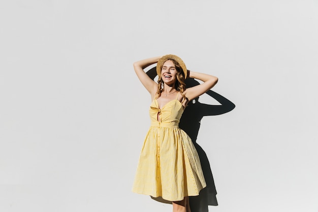 Splendida signora sottile in cappello in posa in una giornata di sole e ridendo. Colpo esterno del modello femminile di buon umore in abito giallo.