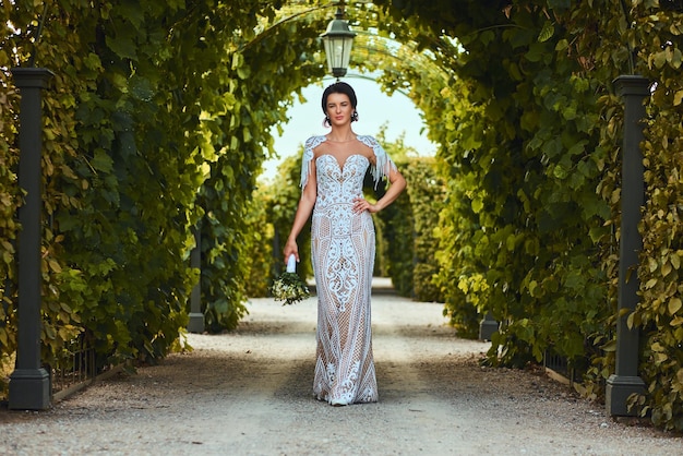 Splendida sposa felice che indossa un bel vestito che tiene il bouquet da sposa e cammina in giardino.