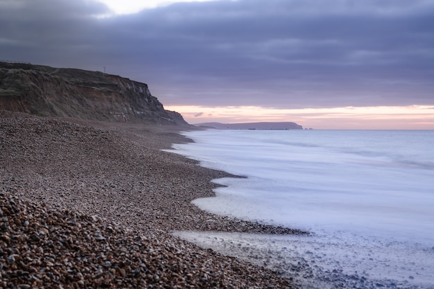 Splendida vista sull'oceano che incontra la spiaggia ricoperta di rocce e ciottoli al tramonto nel Regno Unito