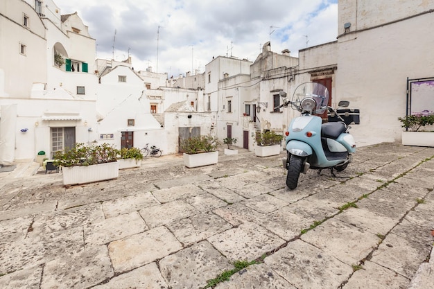 Splendida vista sulle strade vuote del centro storico Martina Franca con belle case dipinte di bianco in mezzo al verde. Ciclomotore blu classico sullo sfondo di edifici antichi. Bella giornata in un tour