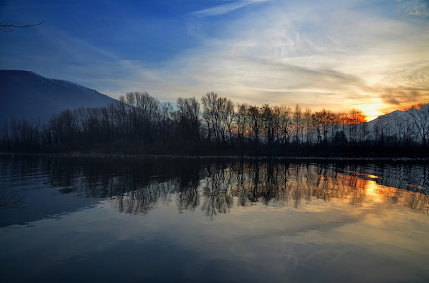 Splendido scenario del tramonto sul lago con sagome di alberi riflessi nell'acqua