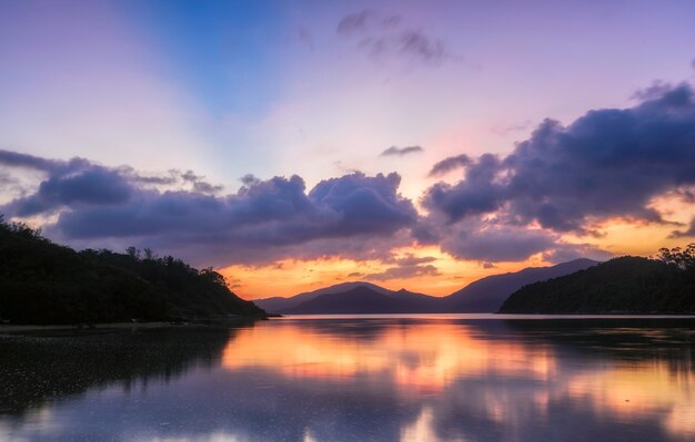 Splendido scenario di un lago circondato da montagne boscose sotto un cielo viola al tramonto