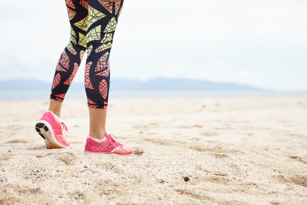 Sport e concetto di stile di vita sano. Ritagliata colpo di gambe di ragazza atleta contro la spiaggia dell'oceano.