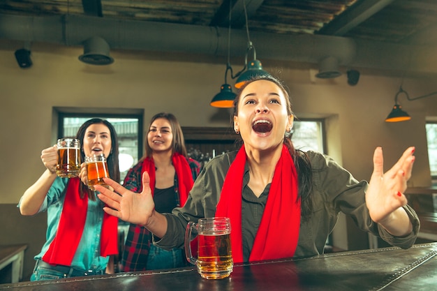 Sport, persone, tempo libero, amicizia, concetto di intrattenimento - tifosi di calcio femminili felici o buoni giovani amici che bevono birra, celebrando la vittoria al bar o al pub. Concetto di emozioni positive umane