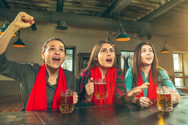 Sport, persone, tempo libero, amicizia, concetto di intrattenimento - tifosi di calcio femminili felici o buoni giovani amici che bevono birra, celebrando la vittoria al bar o al pub. Concetto di emozioni positive umane