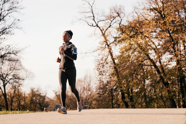 Sportiva afroamericana che corre in natura durante la giornata autunnale Copia spazio