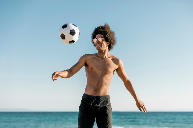 Sportivo afroamericano allegro che gioca a calcio sulla spiaggia