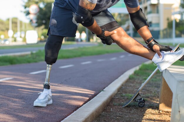 Sportivo con gamba meccanica che si prepara per l'allenamento. Uomo in abiti sportivi che si allungano nel parco il giorno d'estate. Sport, concetto di formazione