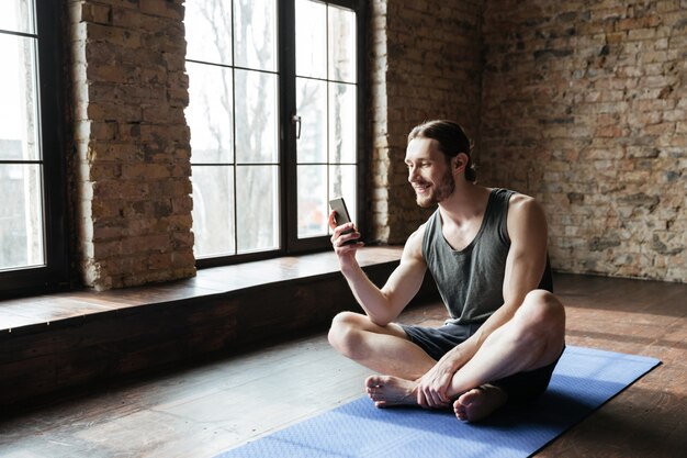 Sportivo concentrato sorridente che per mezzo del telefono cellulare