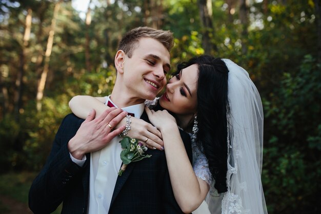 Sposa abbraccia sorridente fidanzato in piedi in legno