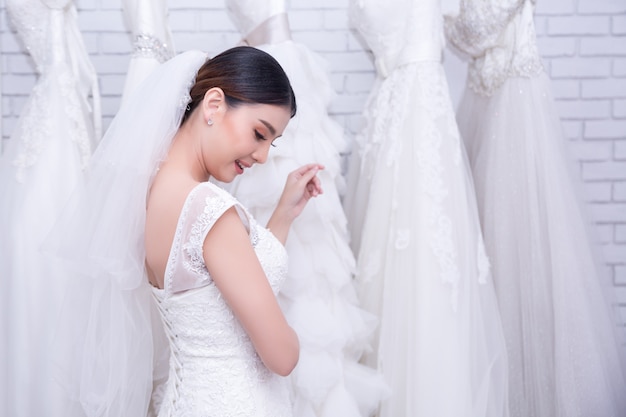 Sposa asiatica della giovane donna che prova sul vestito da sposa alle nozze moderne